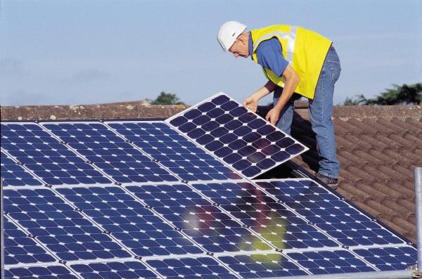 A worker installs solar panels on the roof of a house.